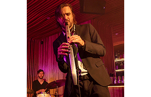 musician playing Roland Aerophone Pro AE-30 on stage with drummer in background