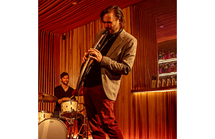 musician playing Roland Aerophone Pro AE-30 on stage with drummer in background