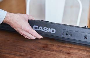 close-up view of musician's hand lifting Casio Casiotone CT-S400 to install batteries