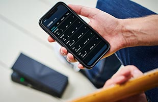 close-up view from above of guitarist's hand holding Bluetooth-connected smartphone running Boss EV-1-WL Editor app with connected Boss EV-1-WL sitting on floor in backgbround