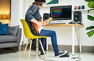 musician playing guitar with Boss EV-1-WL while sitting in front of project studio desk with desktop computer running music recording software