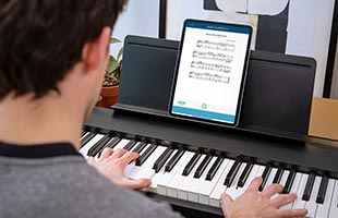 over-the-shoulder image of musician playing Roland FP-30X with Bluetooth-connected tablet computer on music rest