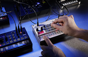 close-up image of hands manipulating controls on Korg Volca Sample 2 with other Volcas surrounding it